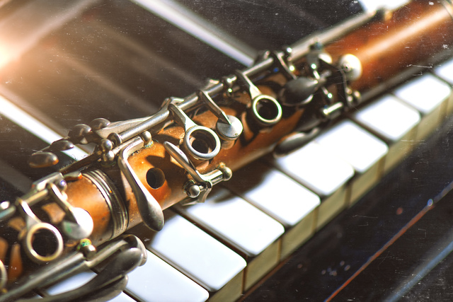 Vintage effect photograph. Antique clarinet leaning on piano keyboard.